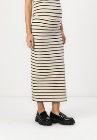 Rochie maxi în dungi, bej și neagră, fabricată dintr-un material moale. Asortată cu loaferi groși negri; textură netedă și formă rotundă.