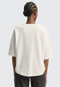 Vit oversized t-shirt med korta ärmar, rundad halsringning, ribbad textur och rak nederkant, i kombination med mörkgrå byxor.