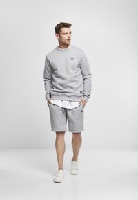 Sudadera gris claro con puños acanalados, cuello redondo y parche de logo, combinada con pantalones cortos grises a juego con cordón ajustable.