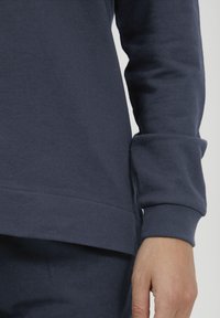 Felpa blu navy in morbido misto cotone, con maniche lunghe, orlo arrotondato e polsini a costine per una maggiore texture.