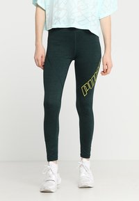 Leggings sportivi verde scuro realizzati in materiale testurizzato, con un logo "PUMA" giallo sul lato e un design aderente.