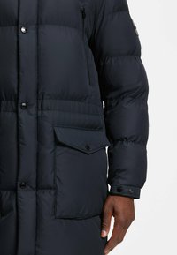 Giubbotto imbottito blu navy con chiusura a button, tasca laterale e superficie tessurizzata. Presenta pannelli cuciti e bottoni a scatto sui polsini.