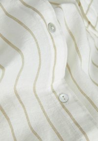 Tejido de lino ligero y blanco con rayas horizontales color crema, que presenta un cierre de botones y detalles de costura visibles.