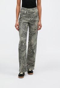 Pantalones de pierna ancha con estampado de cebra en blanco y negro, de talle alto y bolsillos delanteros, combinados con deportivas negras con suela de goma.