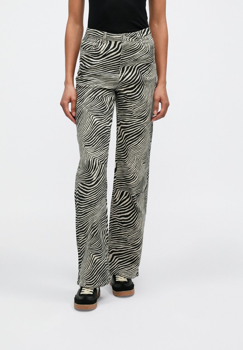 Pantalones de pierna ancha con estampado de cebra en blanco y negro, de talle alto y bolsillos delanteros, combinados con deportivas negras con suela de goma.