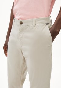 Beige katoenen broek in een katoenmix met een knoopsluiting, riemlussen, zijzakken en een klein merklabel op de tailleband. Gladde textuur.