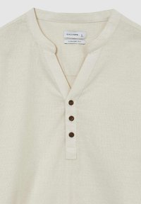Beige Hemd mit Knopfleiste und V-Ausschnitt, drei dekorativen braunen Knöpfen und einem bequemen Schnitt. Hergestellt aus einem weichen, strukturierten Material.