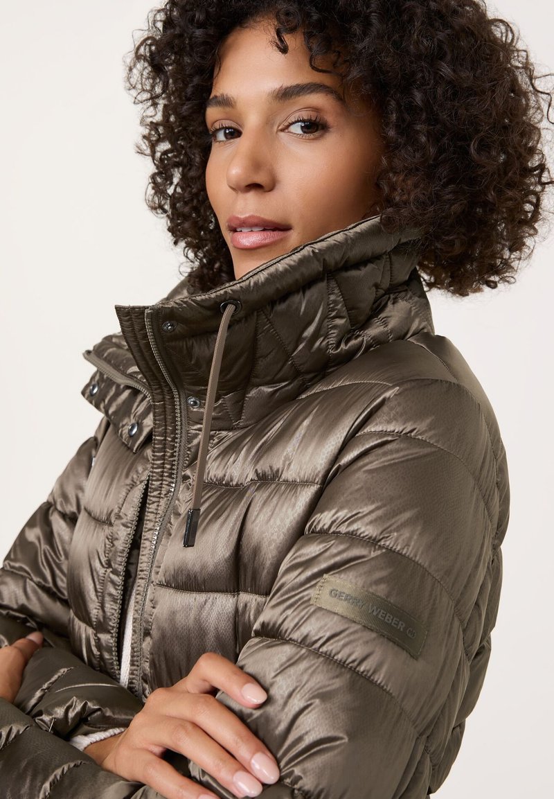 Padded Jacke in metallic olivgrün mit Reißverschluss, hohem Kragen und gesteppten Details. Verfügt über ein Logo-Patch am linken Ärmel.