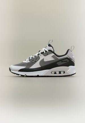 Zijaanzicht van een wit, grijs en zwart Nike Air Max sneaker met zichtbare luchtvering en trek-lussen op de tong en hiel.