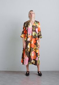 Blomstrete maxikjole med brun bakgrunn og lyse rosa, oransje og grønne blomster, V-hals og trekvartlange ermer.