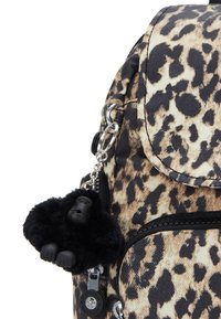 Ryggsäck med leopardmönster, framficka med dragkedja och en svart fluffig gorilla nyckelring fäst vid dragkedjan.