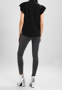 Top negro de manga corta con detalles ondulados, combinado con jeans ajustados grises y botines metálicos con tacones gruesos.