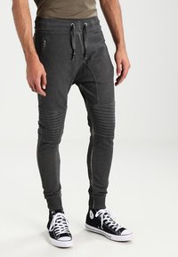 Mörkgrå joggers med ribbade knädetaljer och smal passform, med dragkedjorfickor och dragsko i midjan, tillsammans med svarta sneakers.