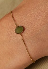 Gouden kettingarmband met een ovale groene steen, gestructureerde zetting en delicate schakels, ontworpen voor een comfortabele pasvorm om de pols.
