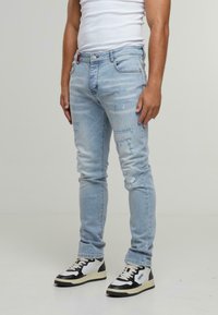 Světle modré obnošené džíny se slim fit, které mají roztrhnutí a pět kapes. Spojené s černo-bílými vysokými teniskami.