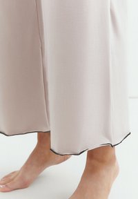 Jasnoróżowe, szerokie spodnie z gładkiego materiału, z falbankowym dołem wykończonym czarnym ściegiem, sięgające powyżej bosej stopy.