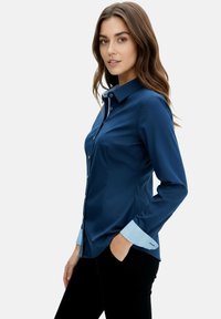 Navy long-sleeve shirt with a button-down collar, featuring striped blue accents on the cuffs, made from a smooth fabric with a tailored fit.