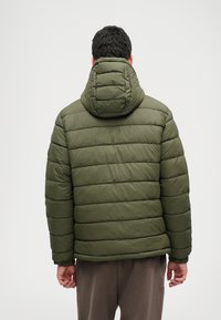 Zöld, kapucnis, párnázott dzseki, vízszintes steppelésű dizájnnal és rugalmas mandzsettákkal. Az anyag simának és vízállónak tűnik.