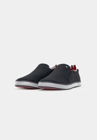 Paire de chaussures décontractées noires sans lacets avec semelles blanches et doublure intérieure rayée rouge, blanche et bleue sur fond uni.