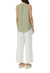 Haut sans manches vert clair avec un col volé, associé à un pantalon large blanc et des sandales à plateforme beiges. Texture de tissu lisse.
