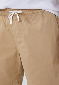 Helle Shorts aus leichtem Stoff, mit einem elastischen Bund und weißem Kordelzug, Seitentasche und glatter Textur.