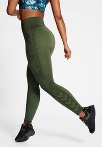 Gröna sportleggings med texturerade paneler och chevronmönster längs sidorna, tillsammans med svarta sportskor.