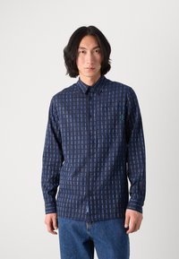 Camisa de botones azul marino con un patrón de cuadrícula en azul claro. Presenta un bolsillo de parche, mangas largas y un cuello estructurado. Textura de tela suave.