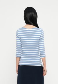 Μπλε και λευκή ρίγα μακρυμάνικη μπλούζα με στρογγυλή λαιμόκοψη και μισοχρόνια μανίκια, συνδυασμένη με μια σκούρα ναυτική υφασμάτινη φούστα.