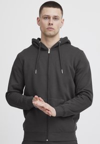 Donkergrijze zip-up hoodie gemaakt van zachte stof. Voorzien van een capuchon met trekkoord, voorzakken en geribde manchetten. Vlotte textuur en casual ontwerp.