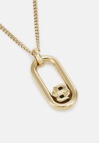 Collier en or avec un grand pendentif ovale présentant un "B" stylisé au centre, suspendu à une chaîne torsadée.