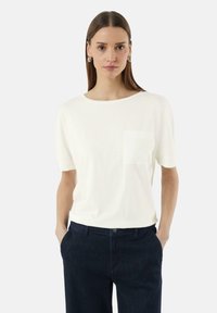 Witte T-shirt met korte mouwen en ronde halslijn, voorzien van een voorzak en gecombineerd met donkerblauwe broek. Soepele textuur en een ontspannen pasvorm.