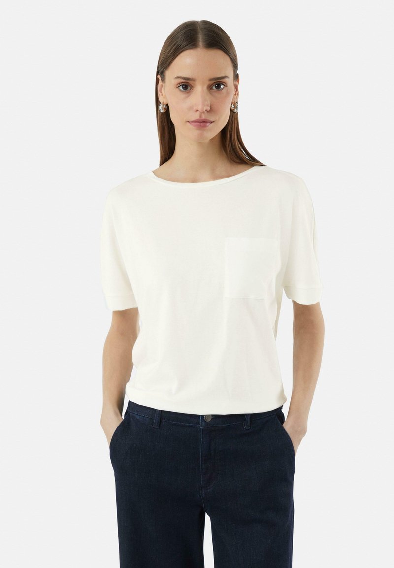 Witte T-shirt met korte mouwen en ronde halslijn, voorzien van een voorzak en gecombineerd met donkerblauwe broek. Soepele textuur en een ontspannen pasvorm.