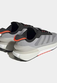 Paire de chaussures de sport grises et noires avec semelles blanches, languettes orange au talon et fermeture à lacets, vues de dos et de côté.