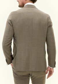Lichtbruin op maat gemaakt colbert met een gladde textuur, enkele split en subtiel patroon. Voorzien van slanke revers en knoopaccenten op de mouwen.