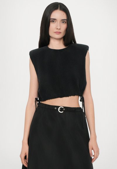 Zwarte cropped top met een ronde halslijn en brede schouders. Zacht materiaal met een rafelige zoom en zijstrikjes. Gecombineerd met een flowy zwarte rok.