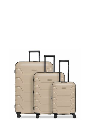 Trois valises rigides beiges de petite, moyenne et grande taille avec des poignées noires et quatre roues chacune, disposées côte à côte.