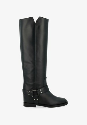Bottes en cuir noir hautes jusqu'aux genoux avec un haut en forme de V, un talon plat et une large sangle ornée d'un anneau en métal et de clous autour de la cheville.