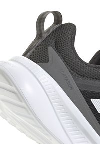 Baskets de course en mesh noir avec une semelle blanche, présentant une tige texturée, des accents gris de soutien et une boucle au talon pour un enfilage facile.