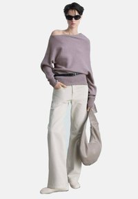 Pulover oversized lavender cu design off-shoulder, asociat cu pantaloni largi crema și o geantă gri lejeră. Ochelarii de soare completează ținuta.