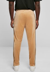 Fluwelen trainingsbroeken in beige met een gladde textuur, voorzien van zwarte zijstrepen en een elastische tailleband. Zachte, taps toelopende pasvorm met een casual fit.