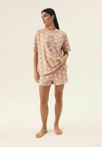 Jasnoróżowy zestaw piżamowy z miękkiego materiału z białymi wzorami chmur. Koszulka z krótkimi rękawami i szorty, obie ozdobione napisem: "DESZCZ TO TYLKO CONFETTI Z NIEBA."