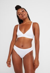 Vit bomullsbalk med djup V-ringning och tunna axelband, i kombination med matchande bikinitrosor med hög midja. Slät, elastisk textur.