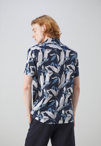 Camicia a maniche corte con sfondo blu navy, caratterizzata da un motivo a foglie in tonalità di blu e bianco. Tessuto leggero con vestibilità rilassata.