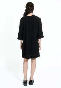 Černé šaty s tříčtvrtečními rukávy, volným střihem, kulatým výstřihem a zipem na zadní straně. Hladká tkanina se rovnou spodní částí.