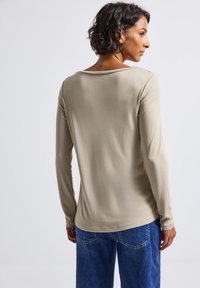Lichtbeige langemouwtop met een ronde halslijn en een zachte textuur, gecombineerd met blauwe denim jeans, gezien vanuit de achterkant.