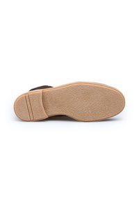 Bruine suede schoen met een tan rubberen zool, met een gestructureerde loopzool en een platte hak. Geen zichtbare logo's of extra details.