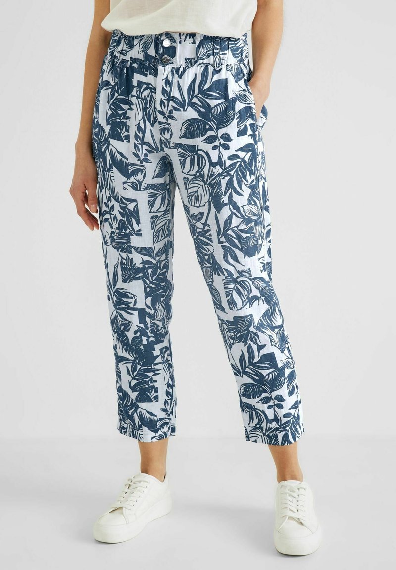 Kalhoty z bavlněné směsi s modro-bílým vzorem listů, s elastickým pasem, bočními kapsami a zkrácenou délkou. Spárováno s bílými teniskami.