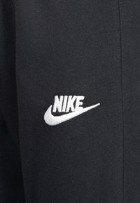 Čierne tepláky Nike s bielym vyšitým logom na ľavej strane, s jemnou textúrou a priliehavým strihom.