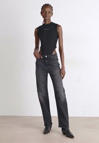 Bodysuit negro con un escote alto y lados cortados, combinado con jeans sueltos de color gris oscuro y botas de tobillo puntiagudas negras.