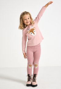 Pink long-sleeve top featuring a deer face design with sequins. Matching pink leggings with deer graphics on the knees. Black lace-up boots.